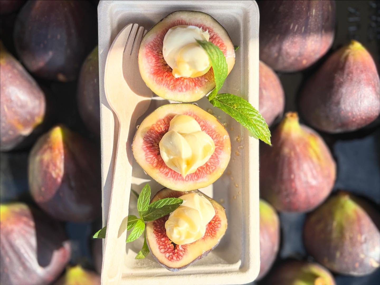 Halved fresh figs on a serving tray surrounded by whole purple figs