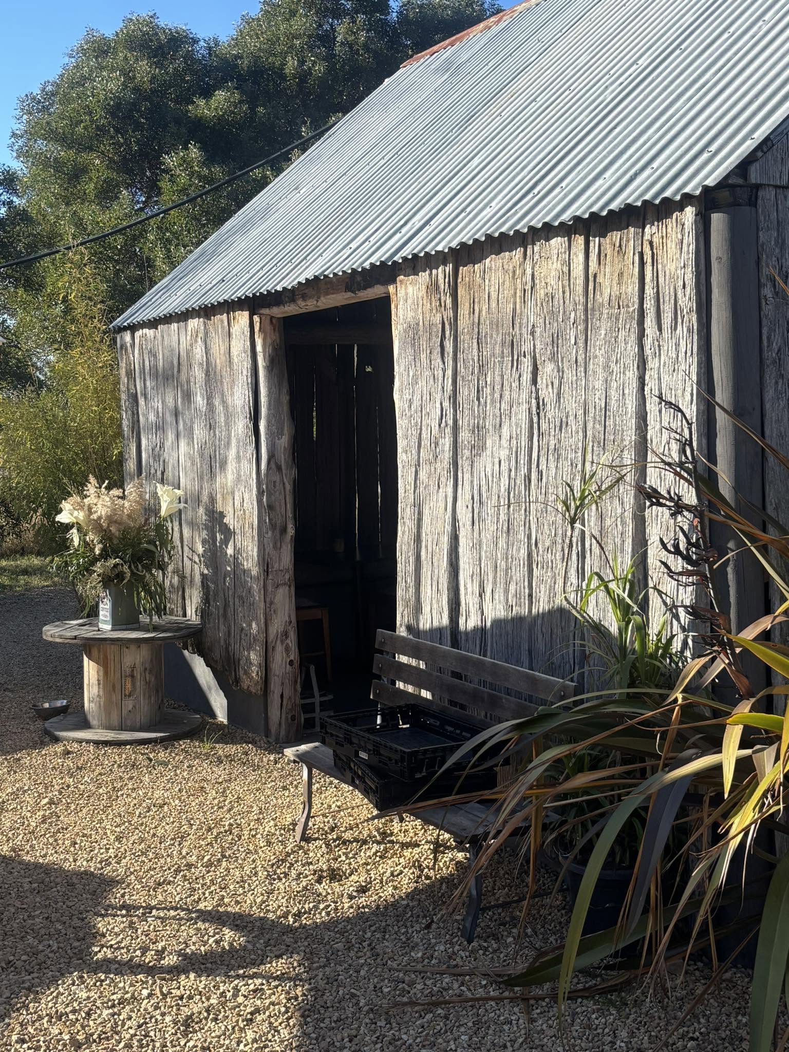 Weathered timber shed with an open doorway, a bench and a cable-spool table